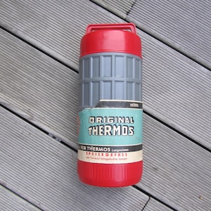 Può includere: Un thermos rosso e grigio con il testo "ORIGINAL THERMOS" e "SPEISEGEFAESS" sull'etichetta. L'etichetta riporta anche "Langewiesen" e "zum Transport fertiggekochder Speisen".
