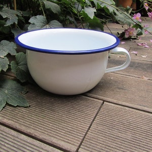 Può includere: Scodella di smalto bianco con bordo blu e manico. La scodella è appoggiata su una superficie di legno.