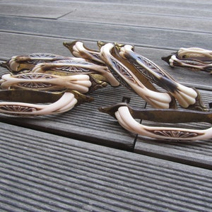 Op de afbeelding: Een groep vintage kastknoppen met een wit keramiek ontwerp en een messing basis. De knoppen hebben een decoratief bloemmotief.