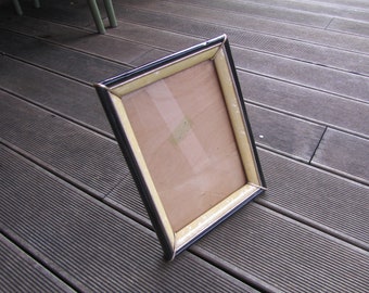 May include: A black and gold picture frame with a beige mat. The frame is lying on a wooden surface.