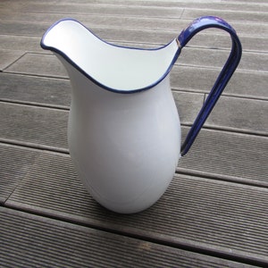 Può includere: Brocca di smalto bianco con bordo e manico blu. La brocca è su una superficie di legno.