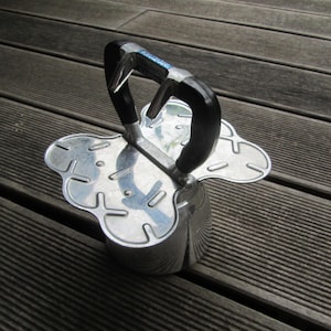 May include: A silver metal kitchen tool with a black handle. The tool has a butterfly-shaped base with multiple holes and a handle that is shaped like a loop.