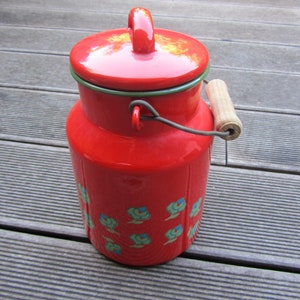 May include: Red enamelware milk can with a wooden handle and a lid. The can has a floral design in blue and green.