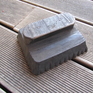 May include: A dark brown wooden tool with a rectangular base and a raised oval top. The base has a row of teeth along the edge.