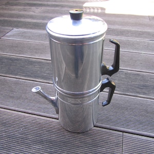 May include: A silver coffee maker with a black handle and a spout. The coffee maker is sitting on a wooden surface.