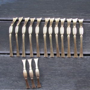 May include: A set of 18 gold-toned cabinet drawer pulls. The pulls are all the same size and shape, with a simple, elegant design. They are arranged in two rows on a wooden surface.