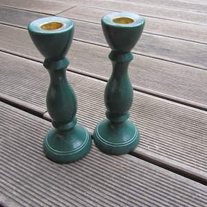 Può includere: Due portacandele in legno verde con cime dorate. I portacandele sono su una superficie di legno.