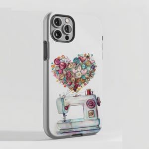 May include: A white smartphone case featuring a graphic illustration of a light blue sewing machine. Above the machine, a collection of colorful buttons and small heart shapes are arranged in the distinct form of a large, central heart.