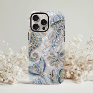 May include: A phone case featuring a pearlescent white background with intricate beadwork designs of a seahorse, jellyfish, octopus, stingray, and fish in shades of blue, gold, and white. The design covers the back of the rectangular case.