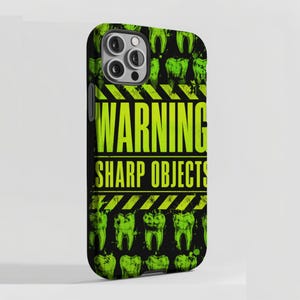 Könnte beinhalten: Eine schwarze Smartphone-Hülle mit einem sich wiederholenden Muster aus lindgrünen Zähnen. In der Mitte steht der Text WARNING SHARP OBJECTS in fetten lindgrünen Buchstaben, umrahmt von gelb-schwarzen Warnstreifen auf schwarzem Grund.