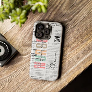 May include: A white iPhone case with a newspaper-style design featuring the words "Registered Nurse" and "RN" in a black and white logo. The case has a black camera bump with three lenses.