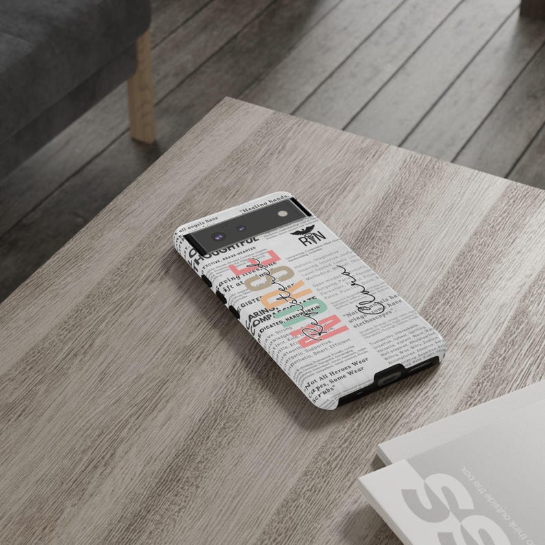 May include: A white phone case with a newspaper print design. The case has a black camera lens and a black bat logo with the text "RIN" printed on it. The case also has the text "Healing Hands" printed on it.