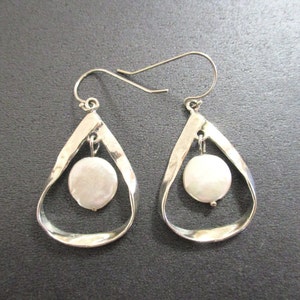 May include: A pair of silver teardrop earrings with a hammered texture. Each earring features a dangling, round, white pearl. The earrings have a simple, elegant design, perfect for everyday wear or special occasions.