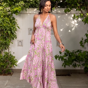 Könnte beinhalten: Ein bodenlanges Neckholder-Kleid mit einem lebendigen, von Paisley inspirierten Blumenmuster in Pink und Grün. Das Kleid hat einen tiefen V-Ausschnitt, dünne Träger zum Binden im Nacken und einen fließenden, lockeren Rock mit geraffter Taille.