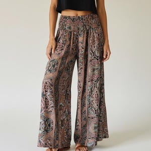 Pode incluir: Uma mulher usando um top preto e calças de perna larga com estampa paisley. As calças apresentam um padrão marrom, preto e verde-azulado. A roupa é completada com sandálias marrons. A roupa é casual e adequada para o clima quente.