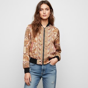 May include: A paisley print bomber jacket in shades of gold, brown, and pink. The jacket has a black zip, cuffs, and hem. The model is wearing blue jeans.