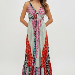 K&ouml;nnte beinhalten: Ein langes, flie&szlig;endes Kleid mit V-Ausschnitt und Spaghettitr&auml;gern. Das Kleid hat ein Patchwork-Design mit verschiedenen Mustern in Rot, Rosa, Blau und Schwarz. Es hat eine betonte Taille und einen Stufenrock.