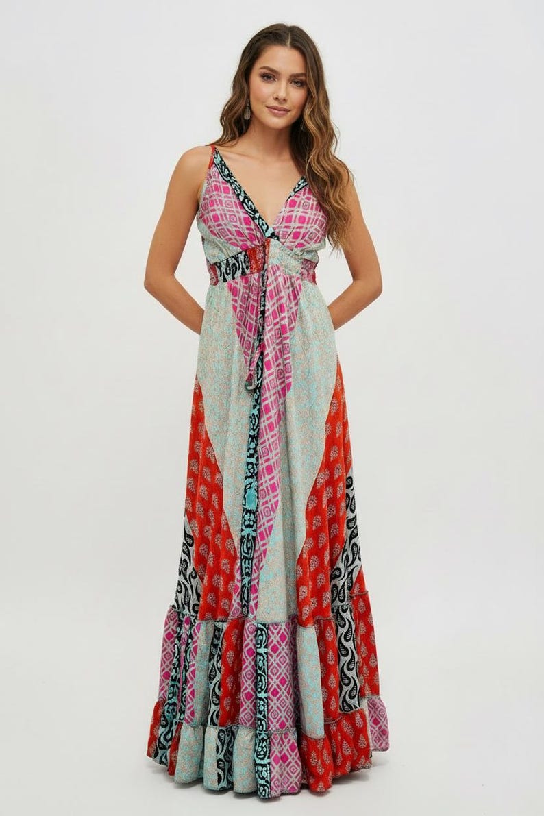 K&ouml;nnte beinhalten: Ein langes, flie&szlig;endes Kleid mit V-Ausschnitt und Spaghettitr&auml;gern. Das Kleid hat ein Patchwork-Design mit verschiedenen Mustern in Rot, Rosa, Blau und Schwarz. Es hat eine betonte Taille und einen Stufenrock.