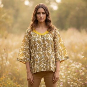 May include: A yellow and cream-colored top with a leaf pattern and a yellow V-neck. The top has wide sleeves and is paired with brown pants. The background is a field of wildflowers.
