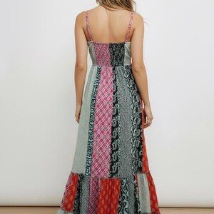 K&ouml;nnte beinhalten: Ein langes, gemustertes Kleid mit Spaghettitr&auml;gern. Das Kleid hat ein Patchwork-Design mit verschiedenen Mustern und Farben, darunter Rosa, T&uuml;rkis, Schwarz und Rot. Das Oberteil ist eng anliegend und der Rock f&auml;llt mit einem R&uuml;schensaum bis zum Boden.