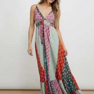 K&ouml;nnte beinhalten: Ein bodenlanges Maxikleid mit Patchwork-Design und verschiedenen Mustern in Rosa, Orange, T&uuml;rkis und Schwarz. Das Kleid hat d&uuml;nne Spaghettitr&auml;ger, einen V-Ausschnitt und einen gestuften Rock mit flie&szlig;ender Silhouette.