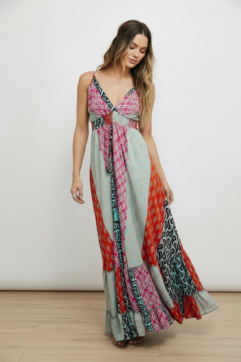 K&ouml;nnte beinhalten: Ein bodenlanges Maxikleid mit Patchwork-Design und verschiedenen Mustern in Rosa, Orange, T&uuml;rkis und Schwarz. Das Kleid hat d&uuml;nne Spaghettitr&auml;ger, einen V-Ausschnitt und einen gestuften Rock mit flie&szlig;ender Silhouette.