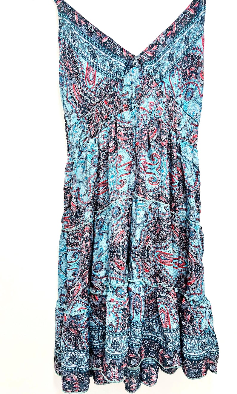 May include: A sleeveless dress with a V-neckline and a tiered skirt. The dress features a paisley pattern in shades of blue, red, and black. The fabric appears lightweight and flowing, suitable for warm weather.