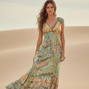 May include: A floor-length maxi dress featuring a vibrant paisley print in shades of teal, orange, yellow, and green. The dress has a V-neckline, short cap sleeves, and a smocked, elasticized bodice that transitions into a tiered, flowing skirt.