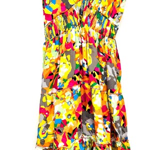 May include: A colorful summer dress with a V-neck and spaghetti straps. The dress features a vibrant abstract pattern in shades of yellow, orange, pink, blue, and gray. The dress has a tiered skirt and elastic waist.