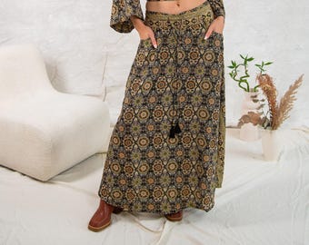 May include: A floor-length skirt featuring a dark base with a repeating intricate geometric floral pattern in shades of gold, orange, and black. The skirt includes a wide waistband with a drawstring closure, two side pockets, and a flared silhouette.