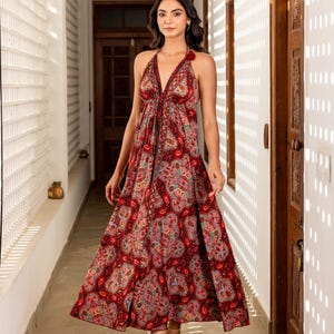 May include: A paisley-patterned midi dress with a halter neck in red, pink, and blue. The dress has a deep V-neck and a flowing skirt. The model is wearing nude sandals.