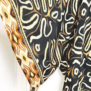 May include: A black garment with a cream and brown abstract pattern. The sleeve edge features a decorative border with geometric shapes in shades of brown and cream. The fabric appears to be lightweight and flowing.