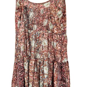 May include: A sleeveless dress with a paisley pattern in shades of pink, brown, and white. The dress features a tiered design with a gathered bodice and spaghetti straps. The fabric has a floral and paisley print.