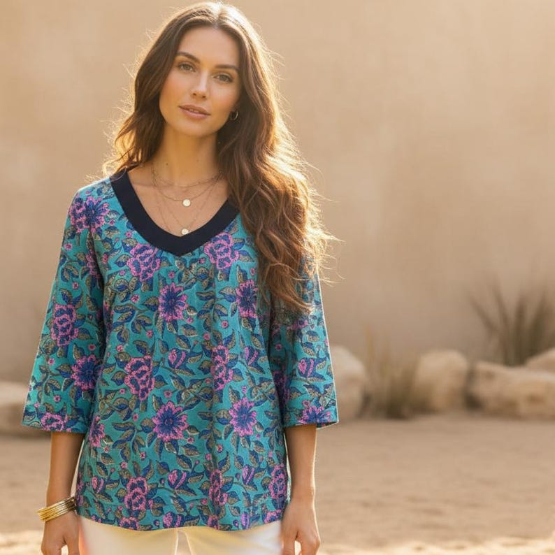 May include: A teal top with a floral pattern in pink and blue. The top has a V-neck with a navy blue trim and three-quarter sleeves. The top is paired with white pants.