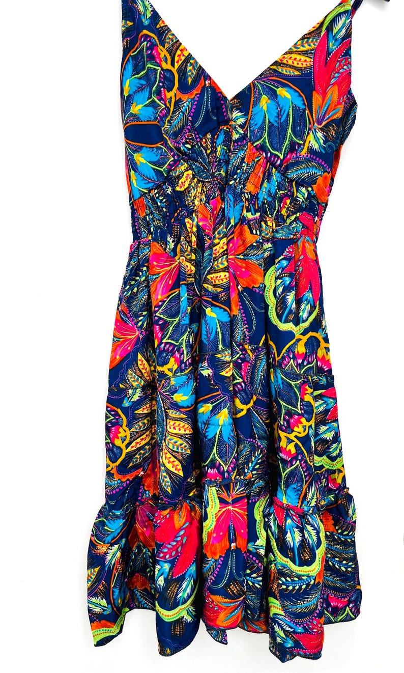 May include: A vibrant, sleeveless dress with a V-neckline and a flowing skirt. The dress features a colorful floral pattern in shades of blue, red, orange, and yellow. The fabric appears lightweight and suitable for warm weather.