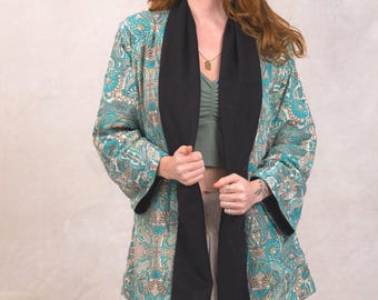 May include: A teal blue and gold patterned kimono with a black scarf. The kimono has a long sleeve and a relaxed fit.