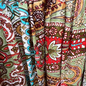 May include: Close-up of a fabric with a paisley pattern in shades of green, red, brown, and white.