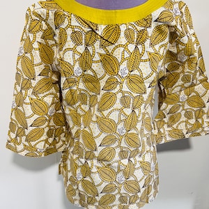 May include: A yellow and white patterned top with a leaf design. The top has three-quarter sleeves and a yellow neckline. The fabric is printed with a repeating pattern of yellow leaves and vines on a white background.