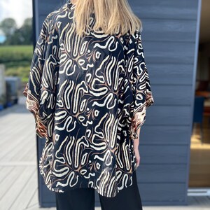 May include: A black kimono-style top with a white and brown abstract pattern. The top has wide sleeves and is paired with black pants. The garment is made of a soft, flowing fabric.