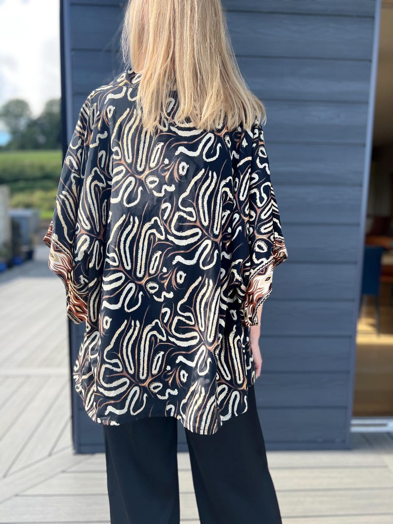 May include: A black kimono-style top with a white and brown abstract pattern. The top has wide sleeves and is paired with black pants. The garment is made of a soft, flowing fabric.