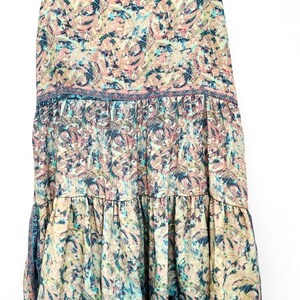 May include: A flowing, tiered dress with spaghetti straps. The dress features a paisley pattern in shades of pink, blue, and cream. The fabric appears lightweight, suitable for warm weather.
