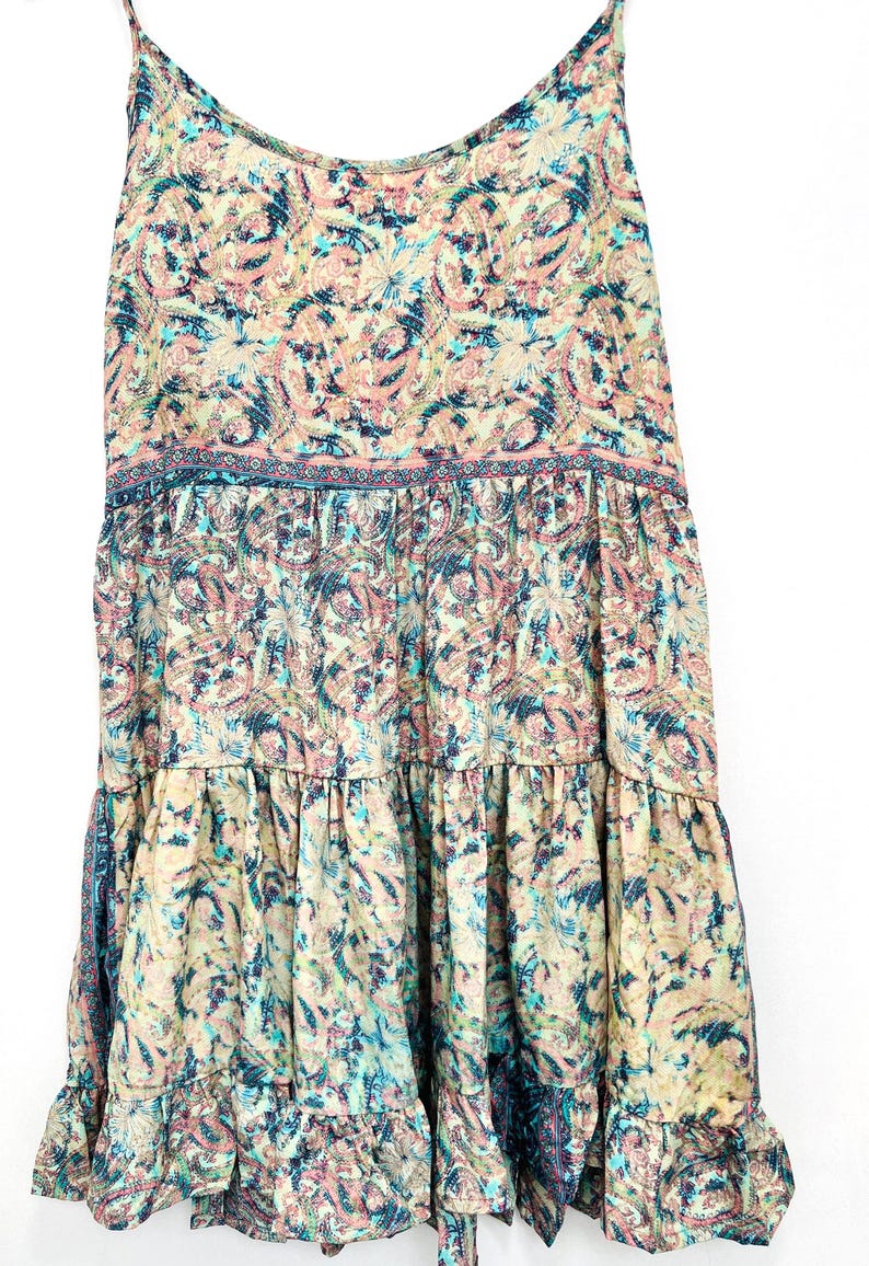 May include: A flowing, tiered dress with spaghetti straps. The dress features a paisley pattern in shades of pink, blue, and cream. The fabric appears lightweight, suitable for warm weather.