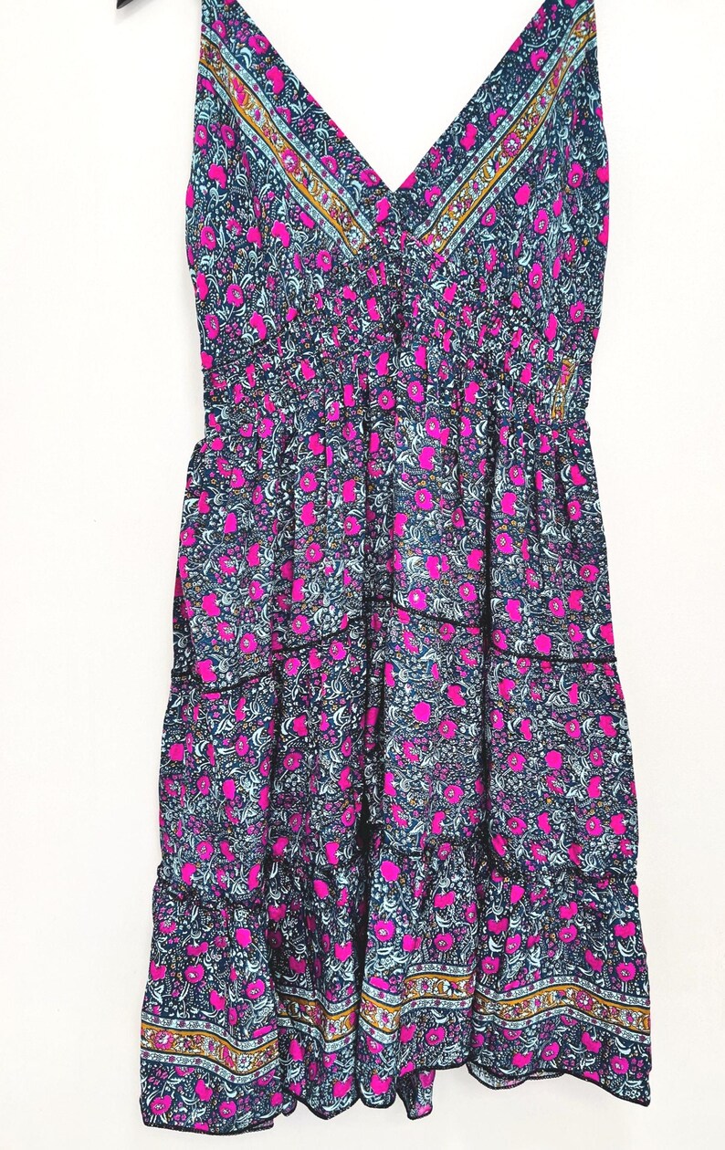 May include: A sleeveless, tiered dress with a V-neckline. The dress features a dark blue background with a floral pattern in pink and light blue. The neckline and hem are trimmed with a decorative border.