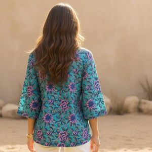 May include: A turquoise floral print top with three-quarter sleeves. The top features a vibrant pattern of pink and blue flowers and green leaves. The garment is made of a lightweight fabric, perfect for warm weather.