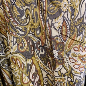 May include: Close-up of a fabric with a paisley pattern in shades of brown, olive green, and cream. The design features floral and teardrop shapes, creating a vintage or bohemian aesthetic. The fabric appears to be soft and flowing.