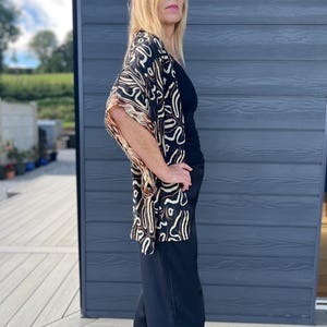 May include: A black top and wide-leg pants are paired with a patterned kimono. The kimono features a black background with a cream and brown abstract design. The outfit is worn outdoors.