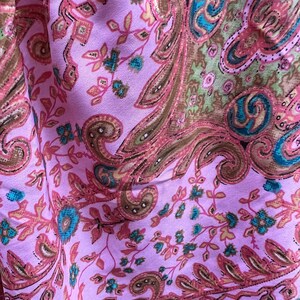 Puede incluir: Primer plano de una tela con un estampado de cachemira. La tela es de color lila claro con un dise&ntilde;o repetido de formas de cachemira y elementos florales marrones, rosas y turquesas. La tela tiene un ligero brillo.