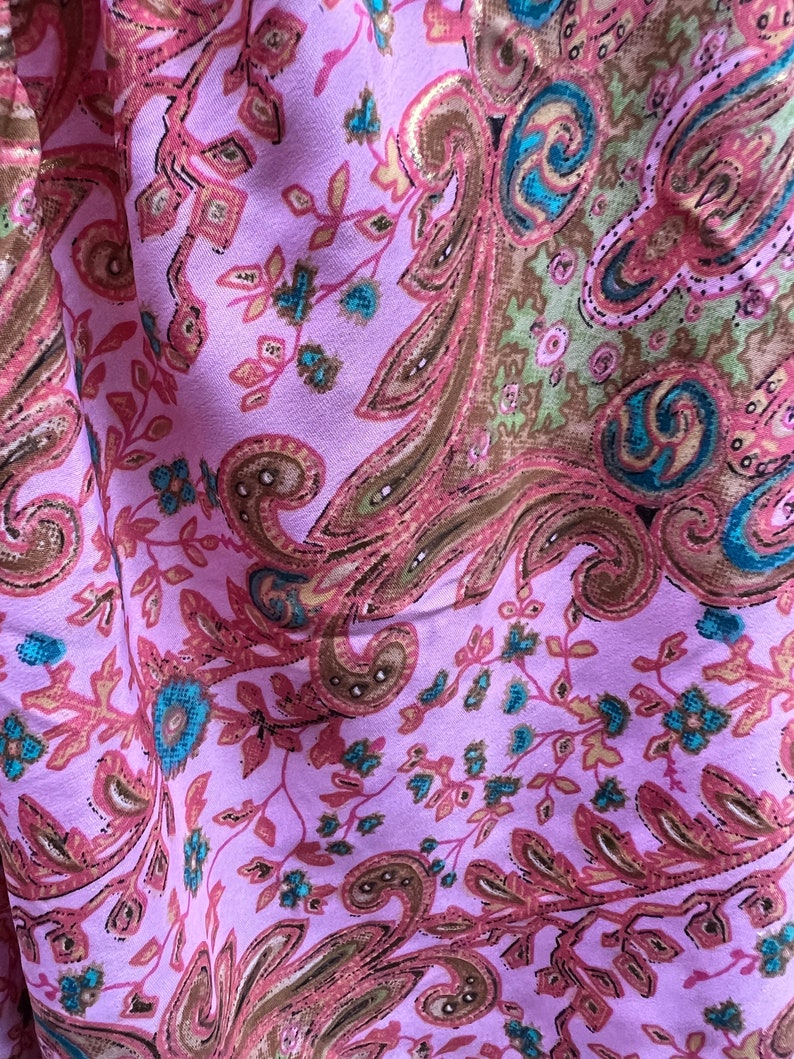Puede incluir: Primer plano de una tela con un estampado de cachemira. La tela es de color lila claro con un dise&ntilde;o repetido de formas de cachemira y elementos florales marrones, rosas y turquesas. La tela tiene un ligero brillo.