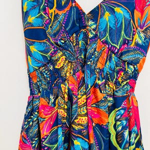 May include: A vibrant, sleeveless dress with a V-neckline. The fabric features a bold floral pattern in shades of blue, orange, pink, and yellow against a dark blue background. The dress has a gathered waist and a flowing skirt.