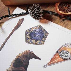 Op de afbeelding: Een witte kaart met illustraties van verschillende Harry Potter-thema-items, waaronder een chocolade kikker doos, een Sorteerhoed, een toverstaf, een fles Felix Felicis en een gouden snitch. De kaart ligt op een houten oppervlak met een dennenappel en een gedroogde sinaasappelschijf.